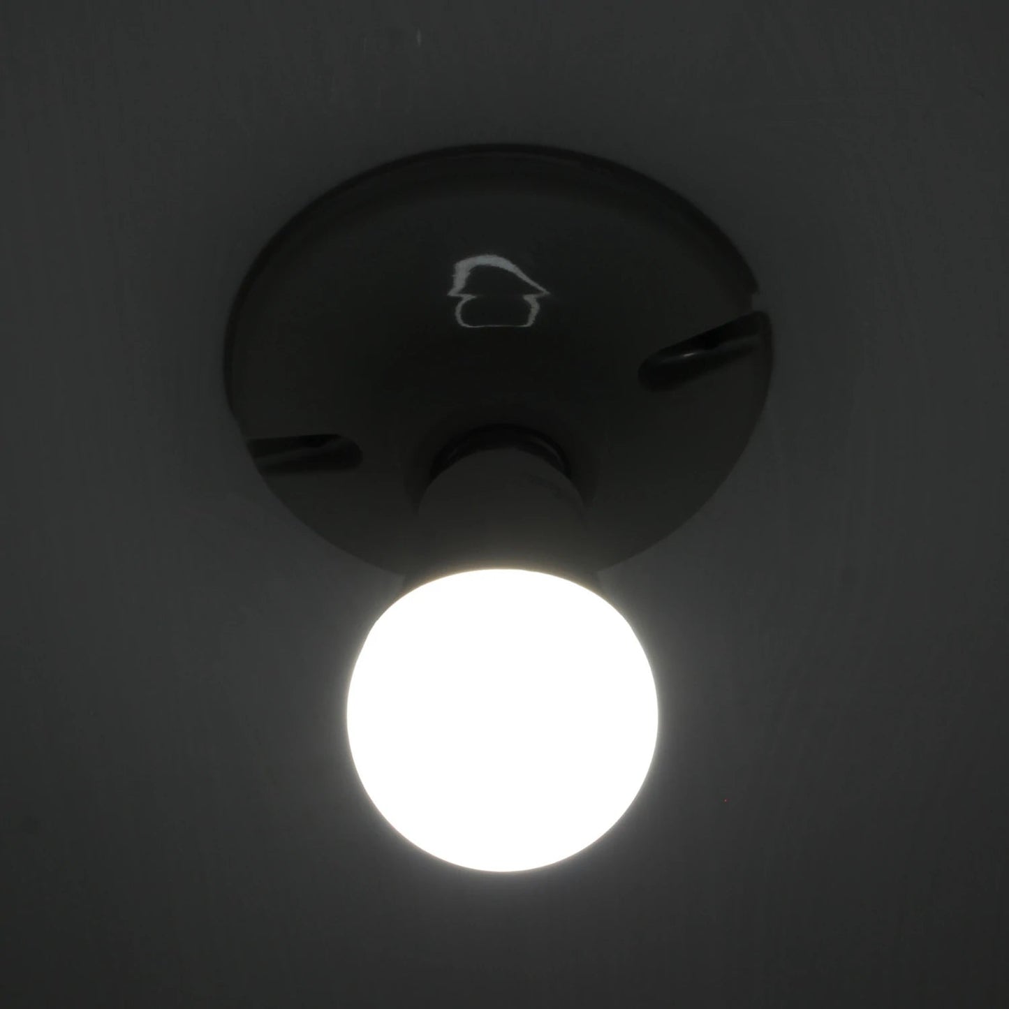 Bombilla LED redonda de luz blanca fría, encendida y brillante, instalada en un plafón oscuro de techo.