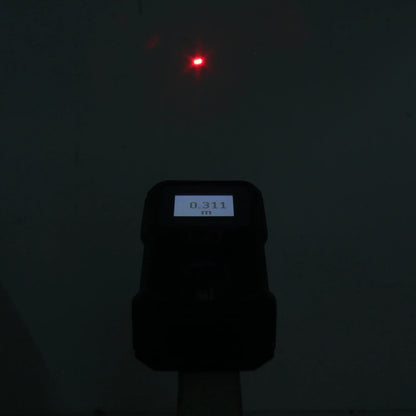 Medidor láser digital proyectando punto rojo, mostrando 0.311m en pantalla para medición de distancia.