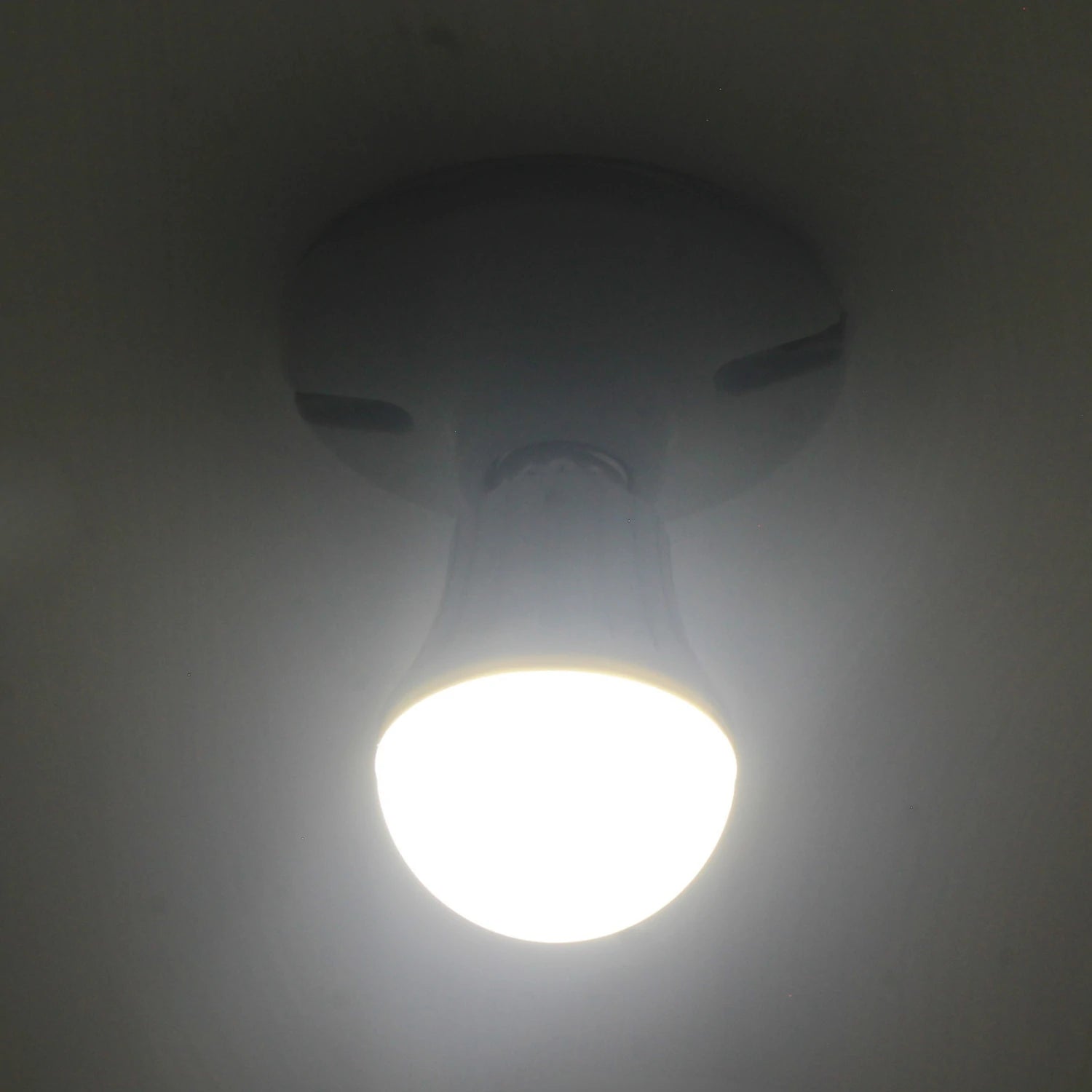 Foco LED tipo bulbo blanco, encendido y emitiendo luz brillante en un plafón de techo.